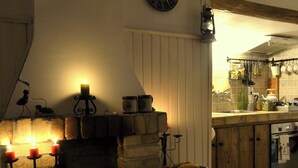 A cozy kitchen with a brick fireplace, a clock on the wall, and various kitchen utensils hanging above the counter. - Villa Markiza - Summer House by the River, at the National Park Central Balkan   (Kalofer)