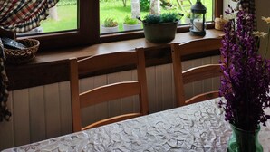 A room with a window overlooking a garden, a wooden table, chairs, and a view of a wooden playhouse. - Villa Markiza - Summer House by the River, at the National Park Central Balkan   (Kalofer)