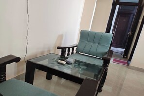 A living room with a glass coffee table, a green upholstered armchair, and a dark wooden sofa. - Hotel Amrapali (Jaipur)
