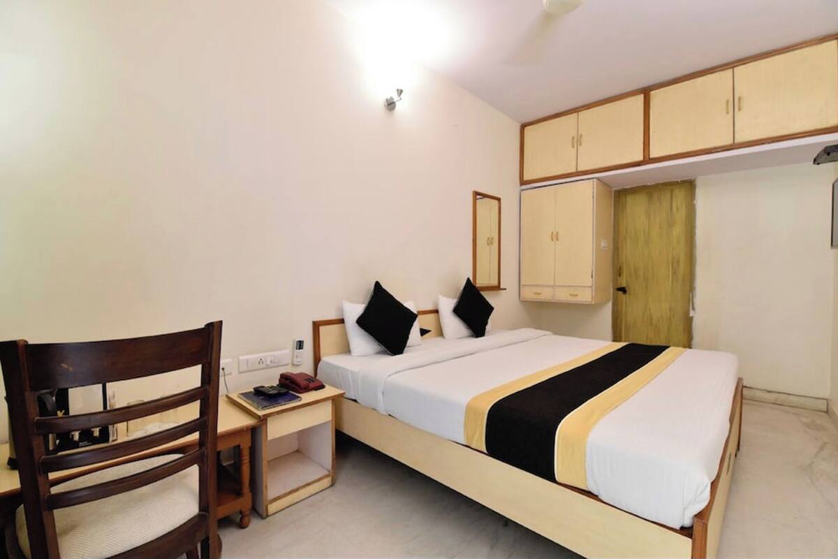 A single bed with a wooden frame, a desk with a chair, a bedside table, and a wardrobe with a mirror.