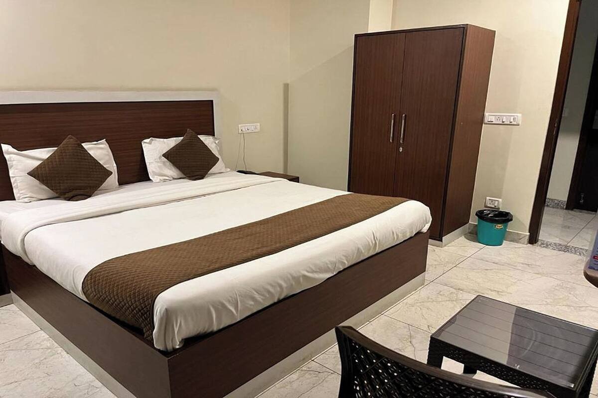 A neatly made bed with a brown headboard and pillows, a wooden wardrobe, and a small table in a hotel room.