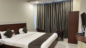 Habitación de hotel con una cama grande, dos sillas, un escritorio con ordenador y televisor.