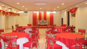 Un salón de conferencias con mesas y sillas redondas, manteles rojos y blancos, y un escenario con un telón de fondo.