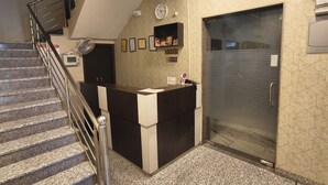 Un área de recepción con mostrador, un reloj, certificados enmarcados y una puerta corredera cerrada.
