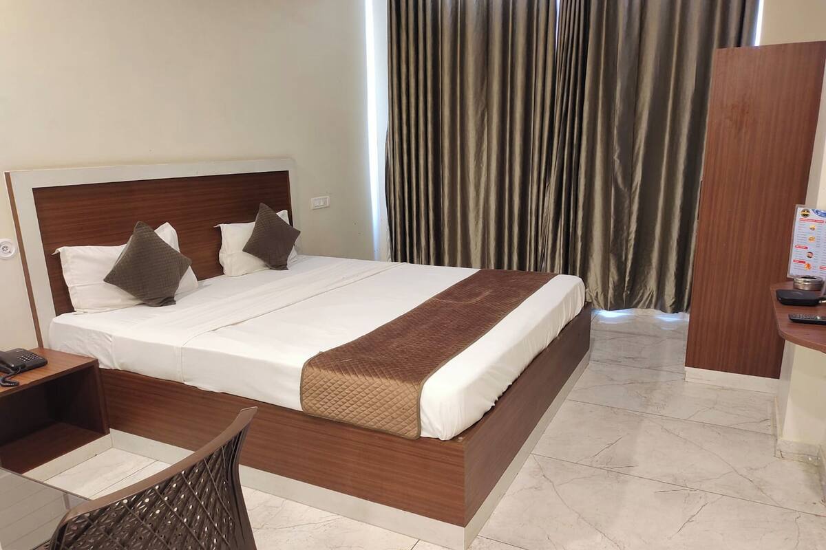 A hotel room with a large bed, a desk with a chair, and a wooden wardrobe.