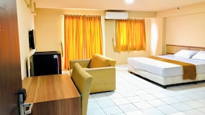 A hotel room with a bed, a desk, a chair, and a small black refrigerator. - Hotel Riau (Bekasi)
