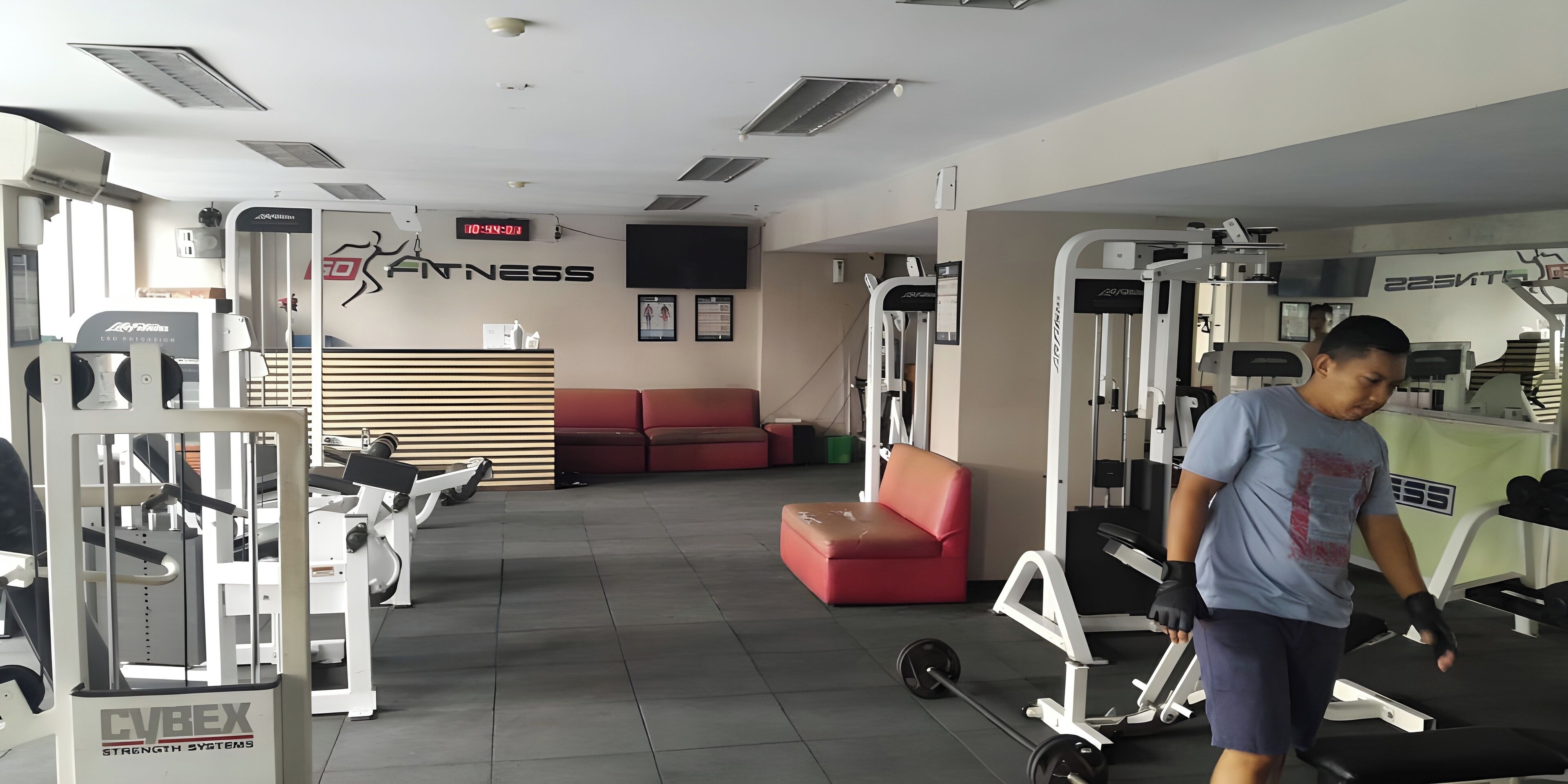 Un gimnasio con diversos equipos de ejercicio, un reloj digital y un sofá rojo.