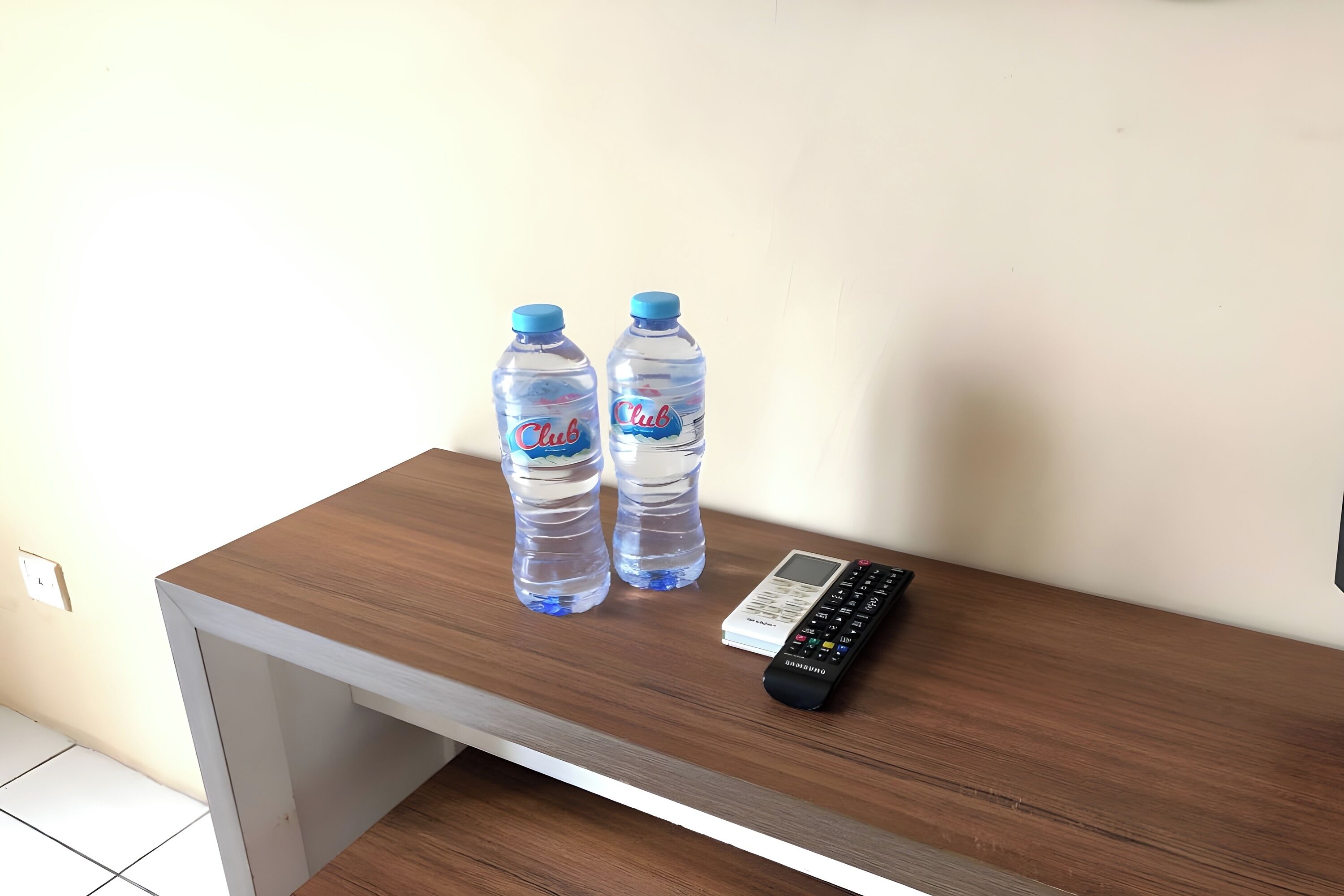 A wooden desk with two Club water bottles and a remote control.