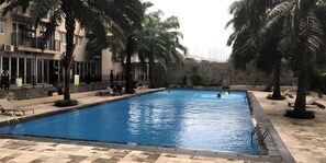 A swimming pool with lounge chairs and palm trees, surrounded by a stone wall and a building with balconies. - Hotel Riau (Bekasi)