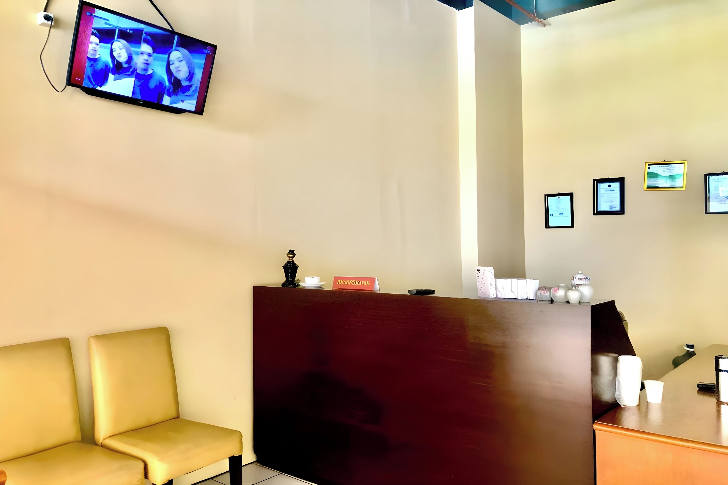 A reception area with a wooden desk, two cushioned chairs, a flat-screen TV, and framed certificates on the wall.
