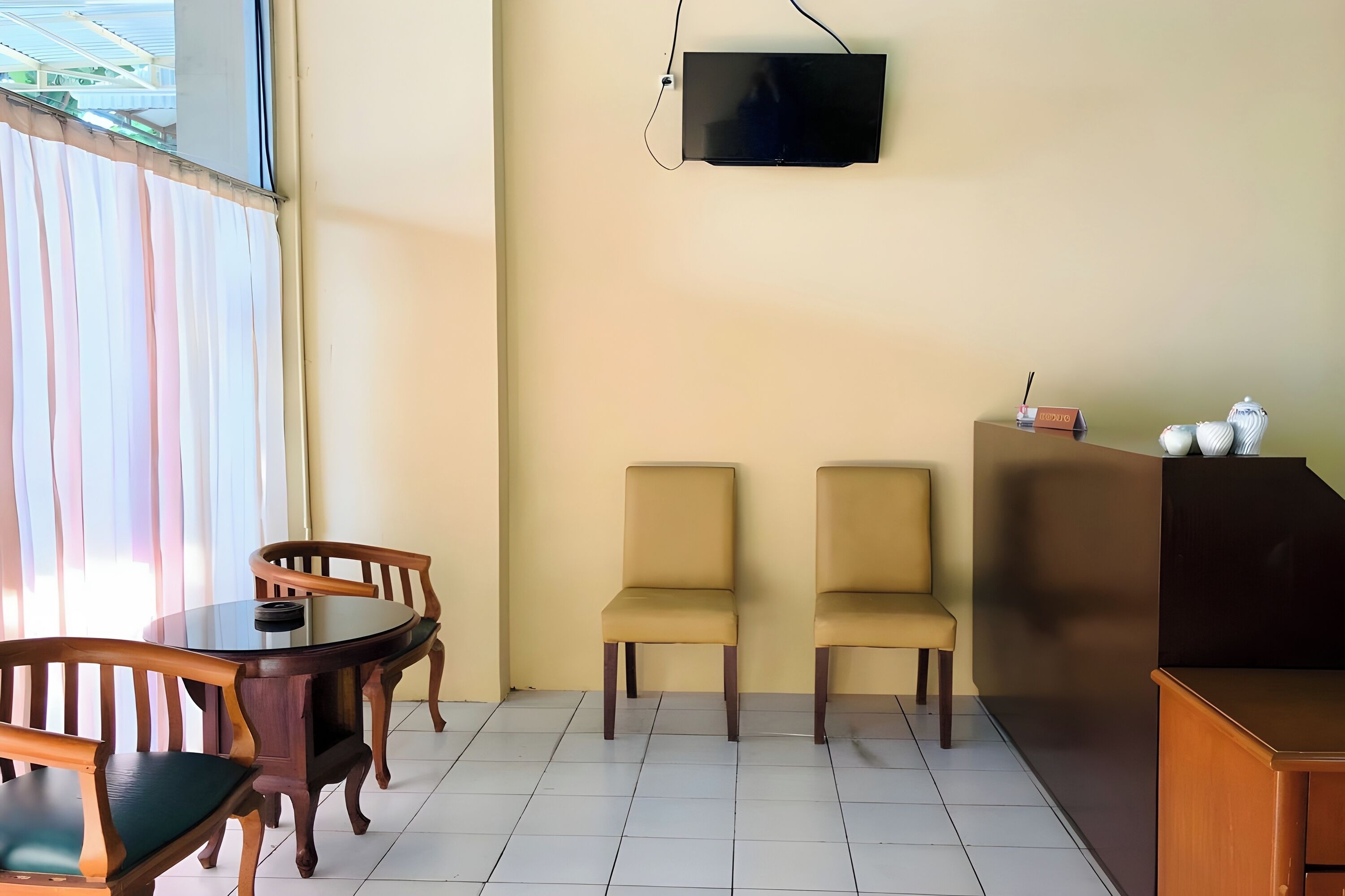 A room with a round wooden table and chairs, a flat-screen TV mounted on the wall, and a small cabinet with a lamp.