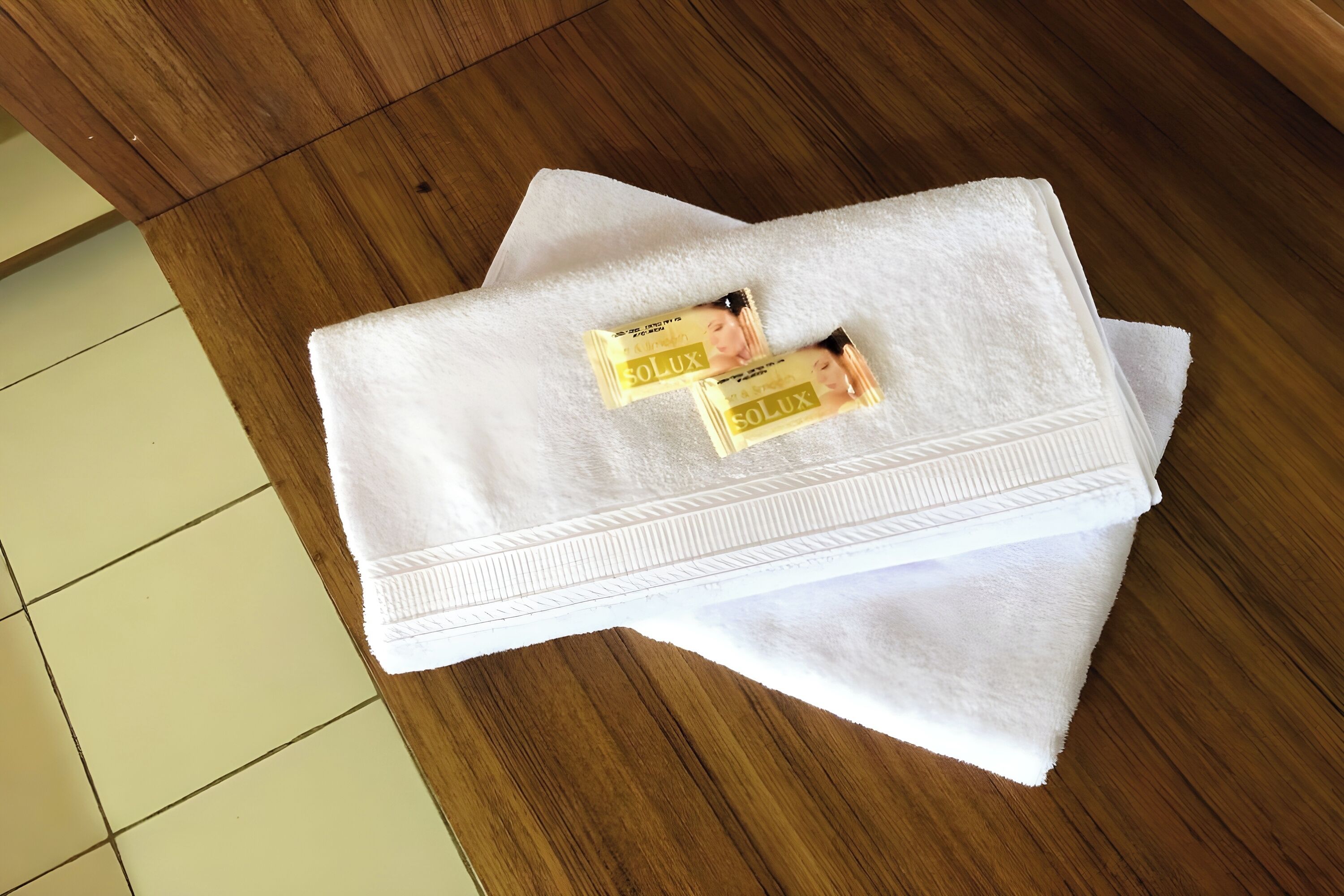 A white towel with two SOLUX bath products on a wooden floor.