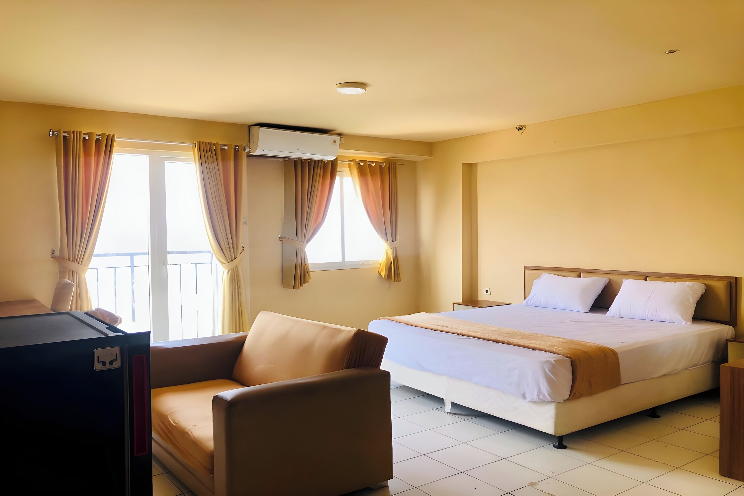 A hotel room with a bed, a chair, an air conditioner, and curtains.