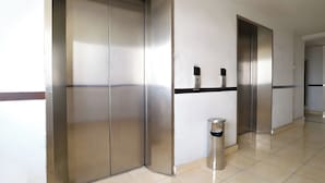 A corridor with two elevators, a trash bin, and a wall with a black stripe. - Hotel Riau (Bekasi)