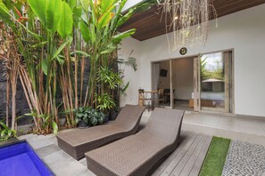 A modern outdoor lounge area with wicker furniture, a stone wall, and lush tropical plants. - Pis Bolong Canggu (Canggu)