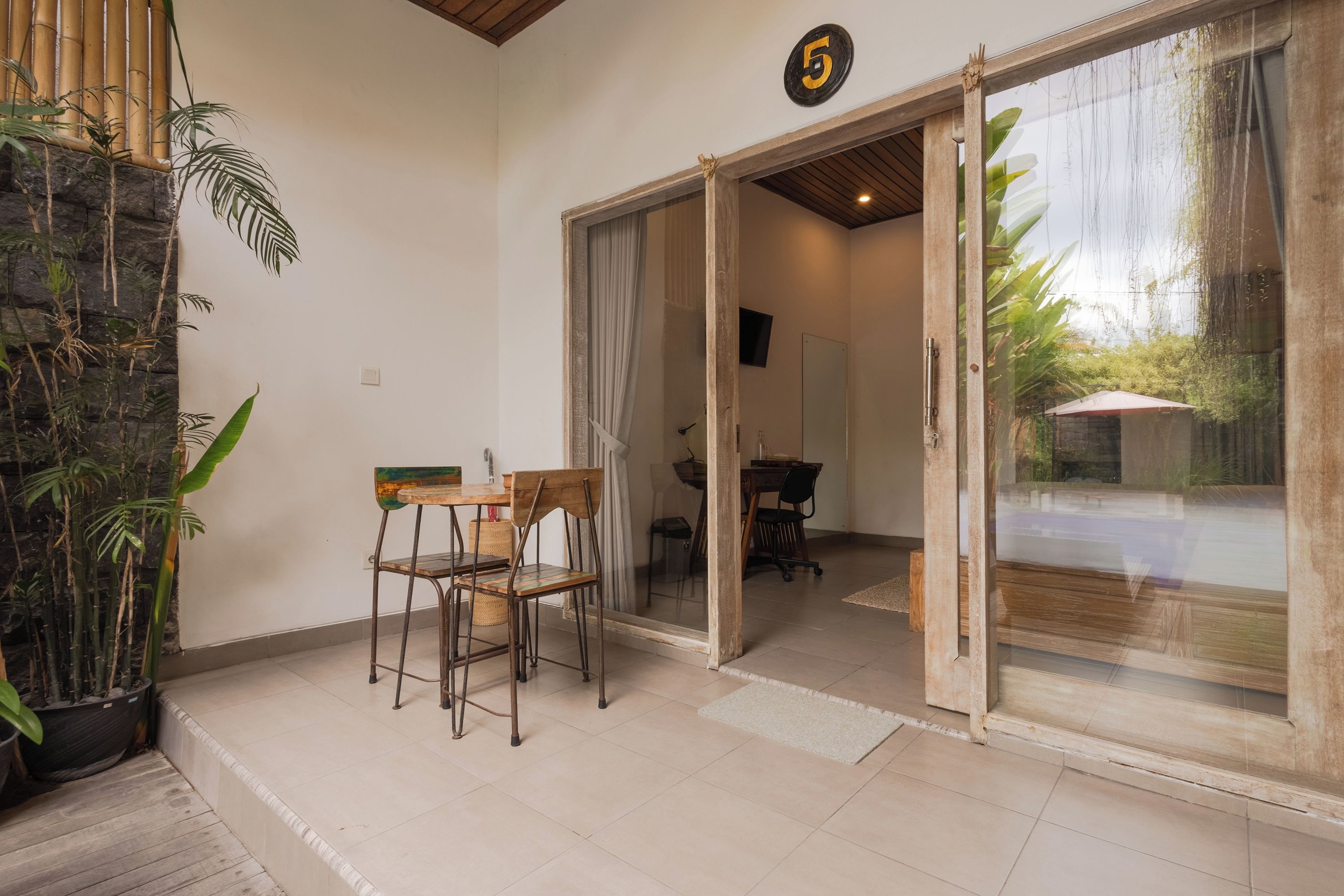A room with a sliding glass door leading to a balcony, a small table with chairs, and a potted plant.