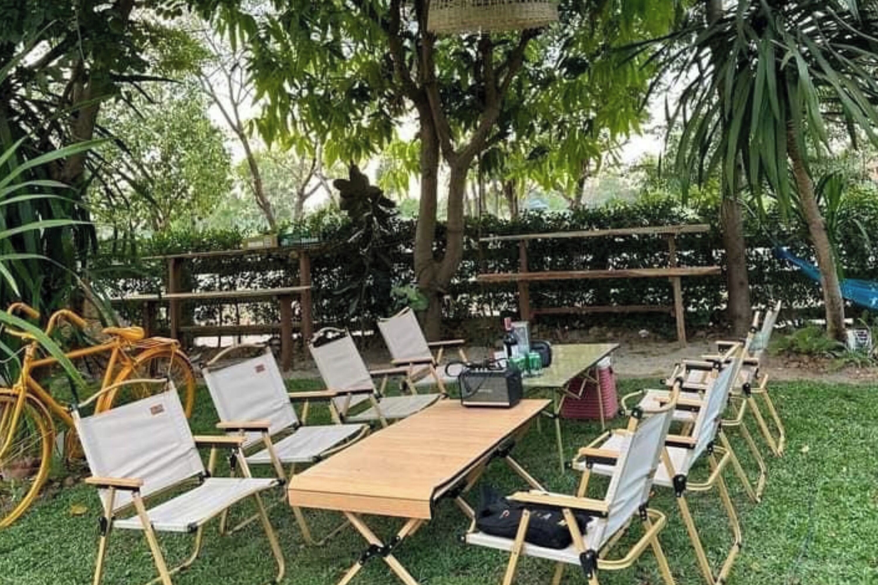 An outdoor seating area with foldable chairs and a table, surrounded by greenery and trees.