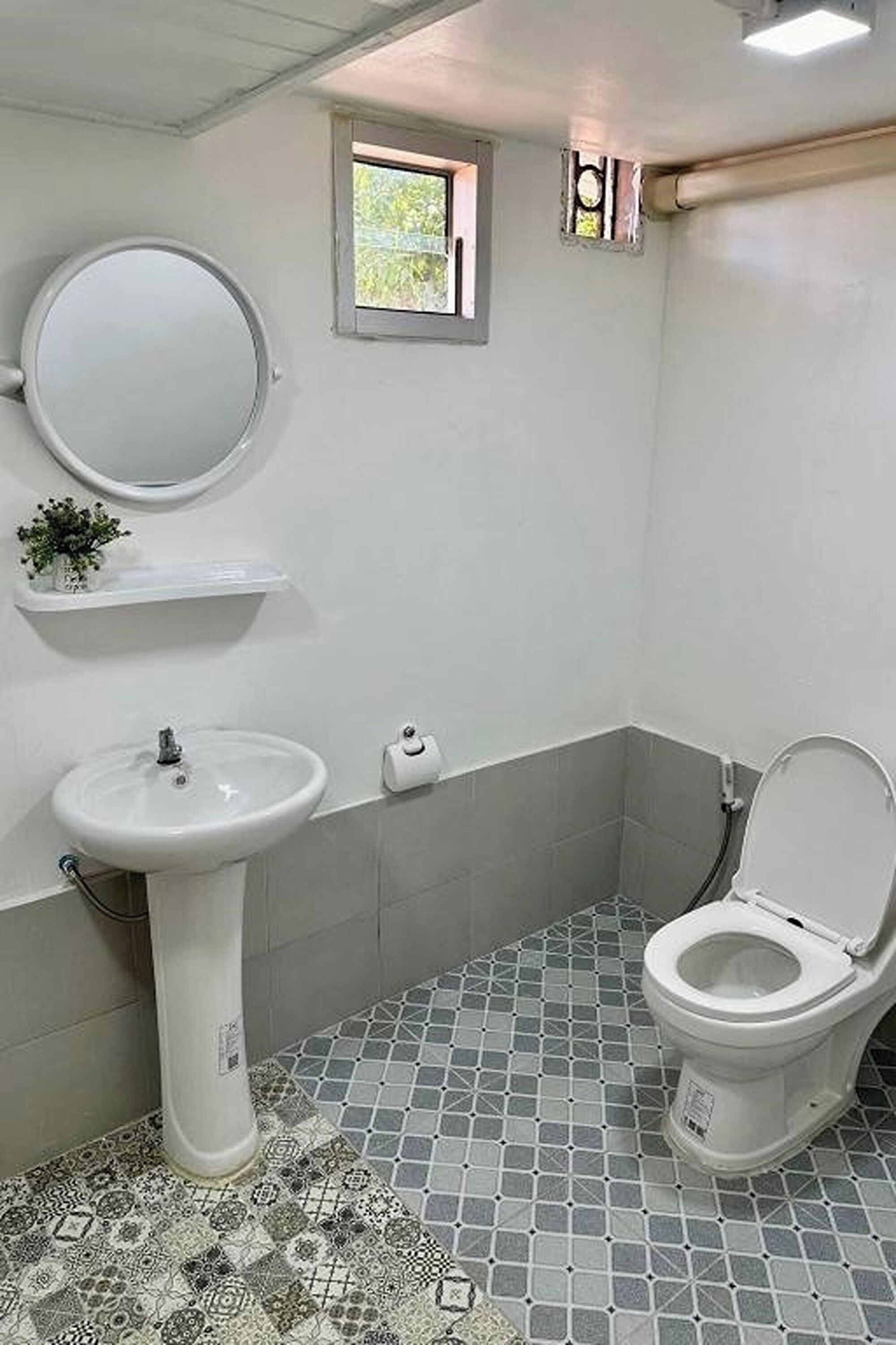 A bathroom with a pedestal sink, toilet, and a small window.