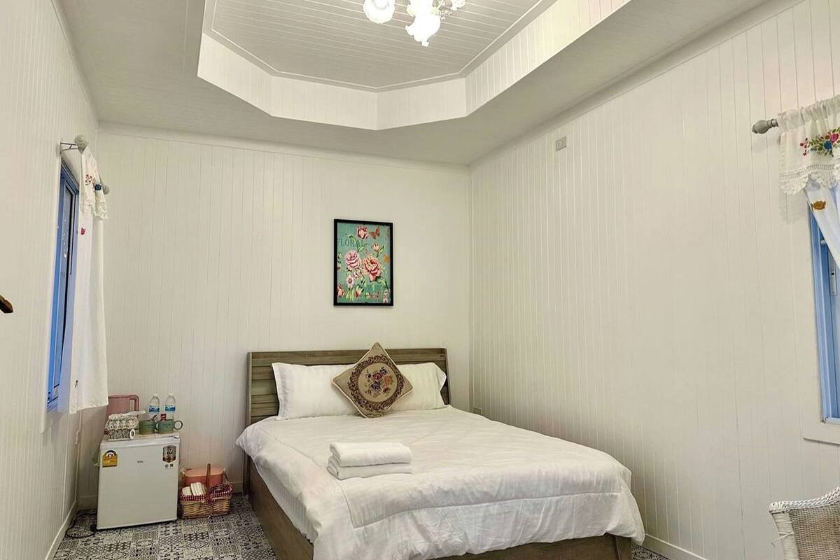 Une chambre avec un lit, un petit réfrigérateur, un panier et un tableau accroché au mur.