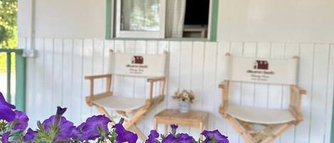 Due sedie di legno con cartelli, un tavolino e fiori viola in primo piano.