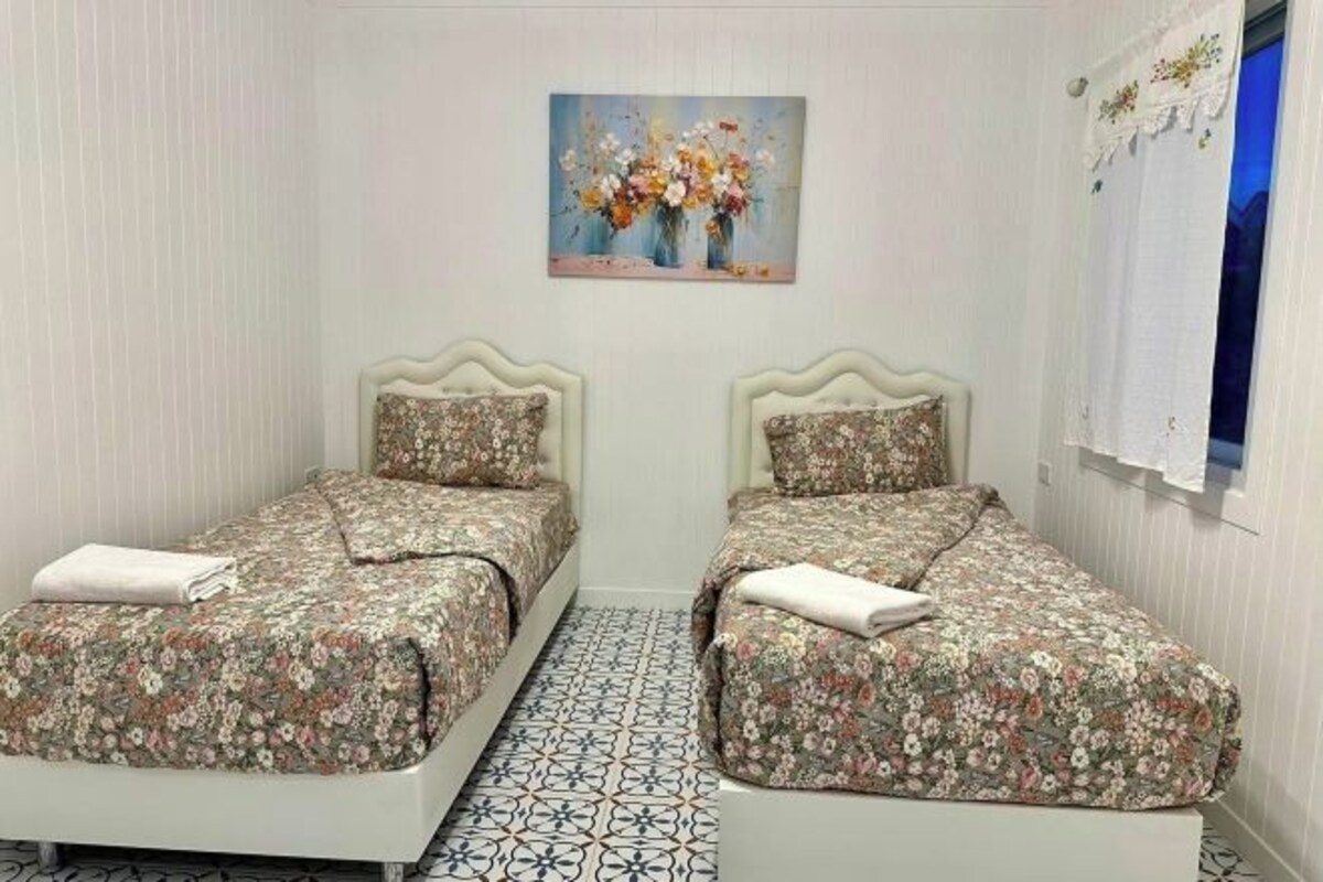 A room with two beds, a painting on the wall, and a window with curtains.