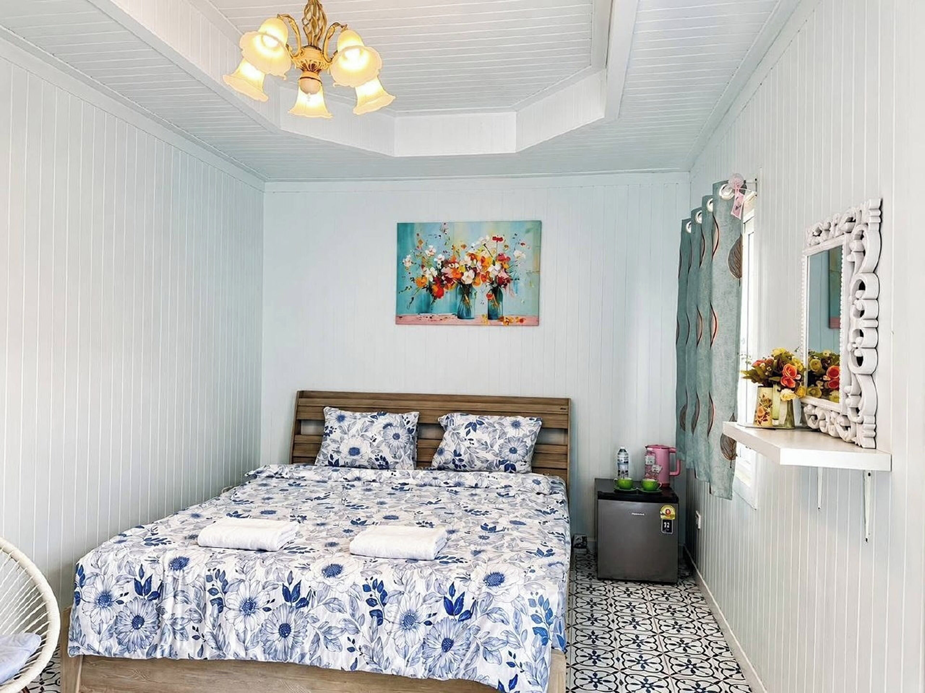 Un dormitorio con cama, un cuadro, un espejo y una mesita con tetera.