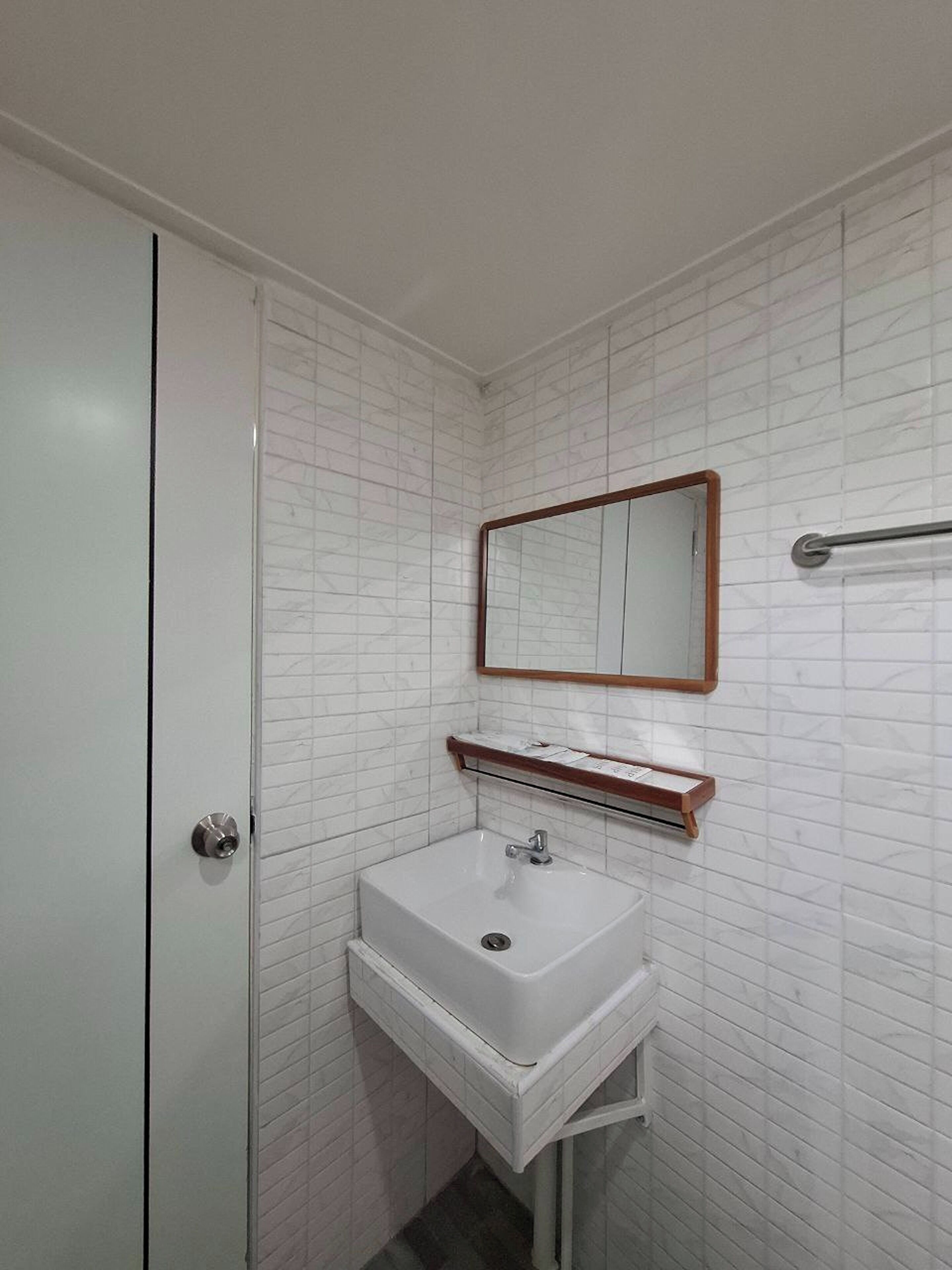 A bathroom with a white tiled wall, a white sink, a mirror, and a towel rack.