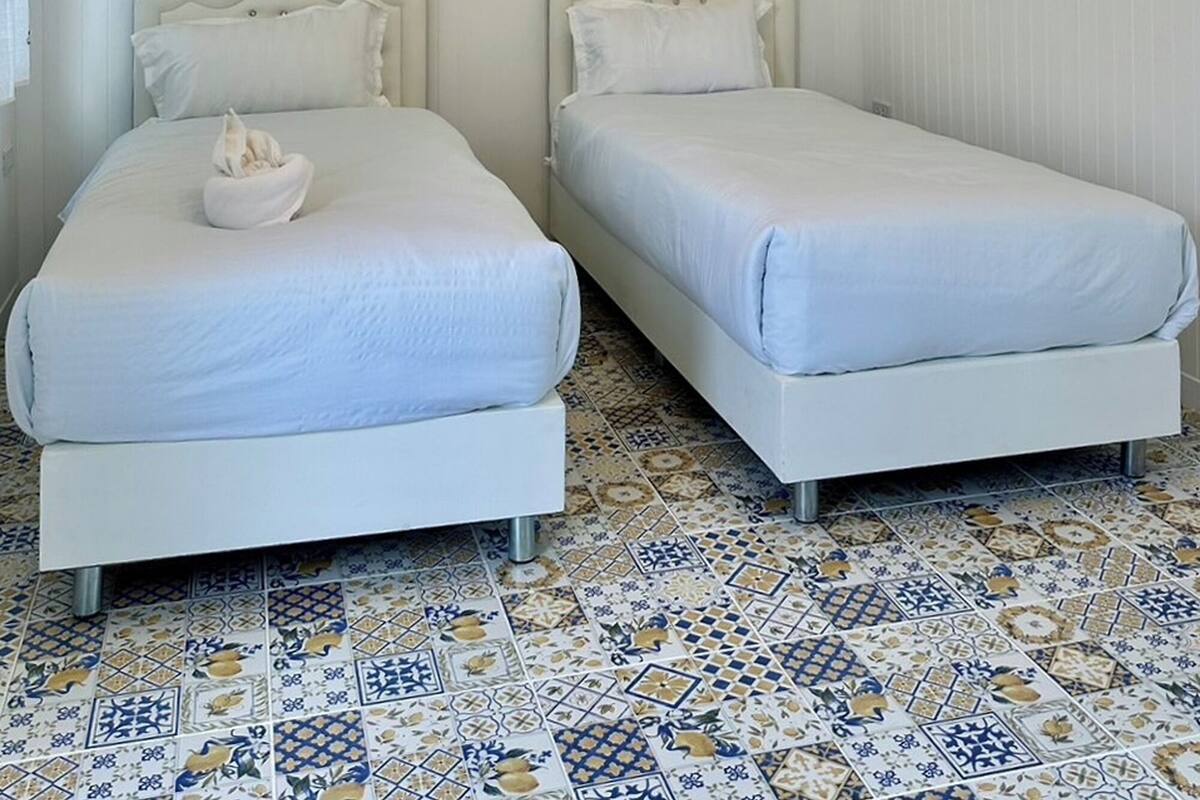 Une chambre avec deux lits, un sol carrelé à motifs et un plafond orné de luminaires suspendus.