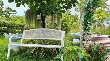 Un banco blanco con respaldo decorativo, rodeado de abundante follaje y diversas plantas.