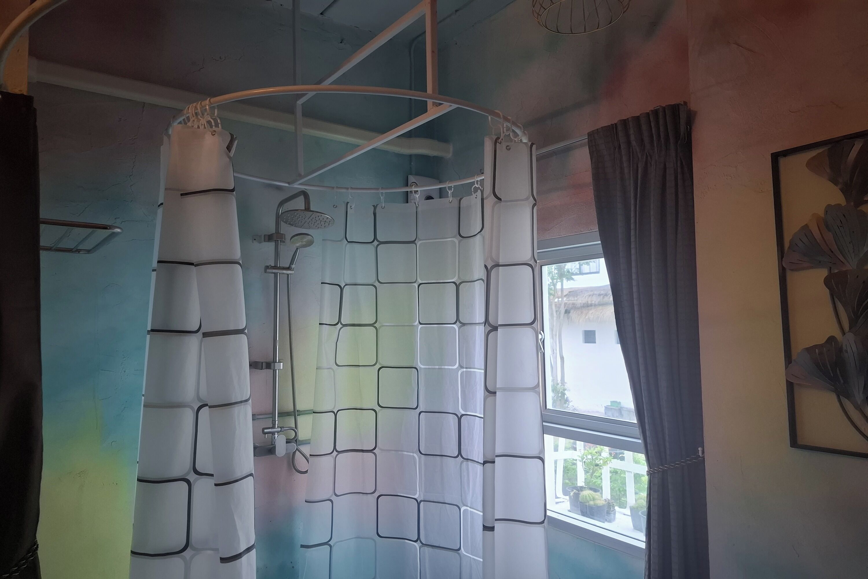 A room with a shower curtain featuring a geometric pattern, a window with a view of the outside, and a framed artwork on the wall.