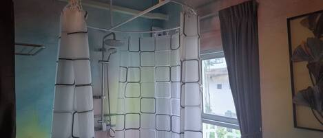 A room with a shower curtain featuring a geometric pattern, a window with a view of the outside, and a framed artwork on the wall.