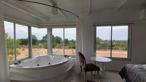 A room with a large bathtub, a bed, a small table, and a chair. There are large windows providing a view of a landscape. - Khao Chi Chan Resort (Sattahip)