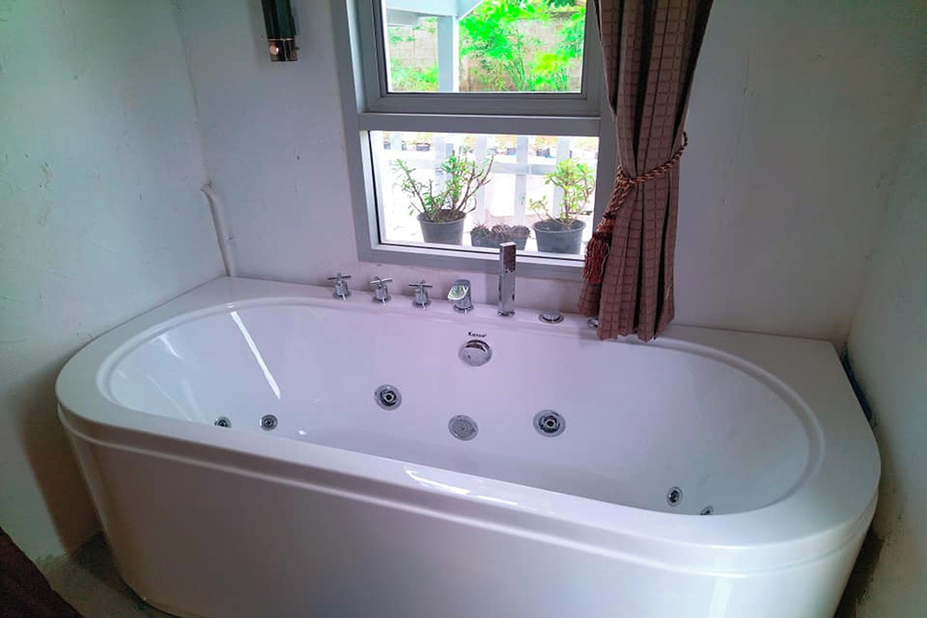 Ein Badezimmer mit einer großen weißen Badewanne, einem Fenster mit Blumentöpfen und einem Vorhang.