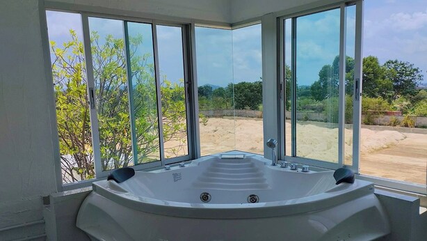A modern bathroom with a large bathtub, large windows, and a view of a sandy area. - Khao Chi Chan Resort (Sattahip)