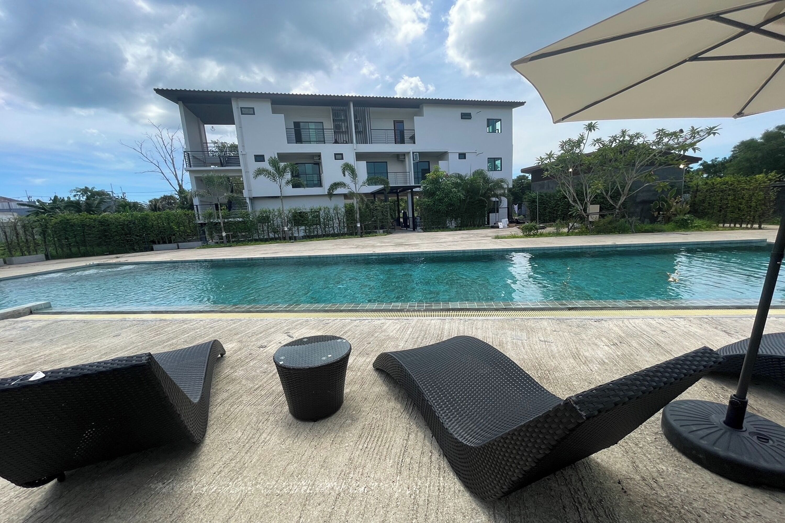 Un bâtiment moderne doté d’une piscine, de chaises longues et d’une petite table.