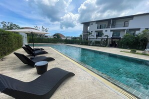 A poolside area with lounge chairs and a table, a clear pool, and a building in the background. - Alisse Stay Phuket Layan (Thep Krasattri)