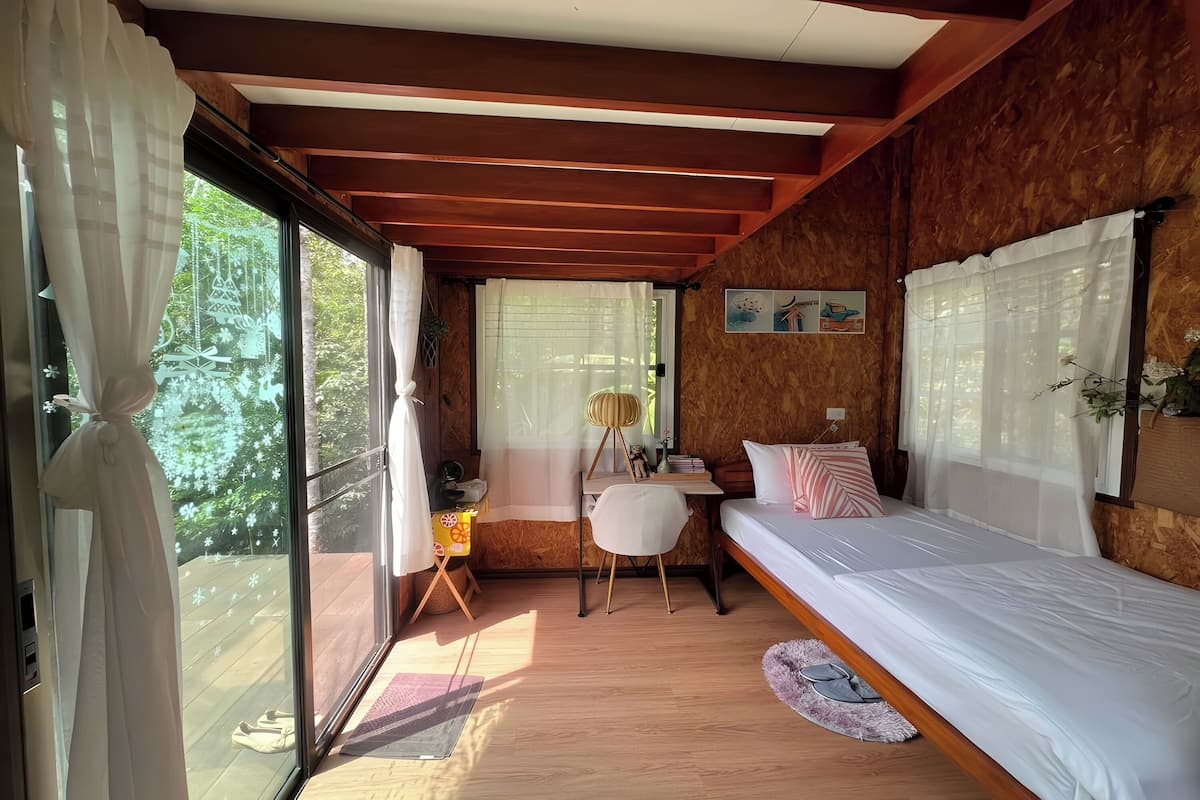 A cozy room with a bed, desk, and large windows.