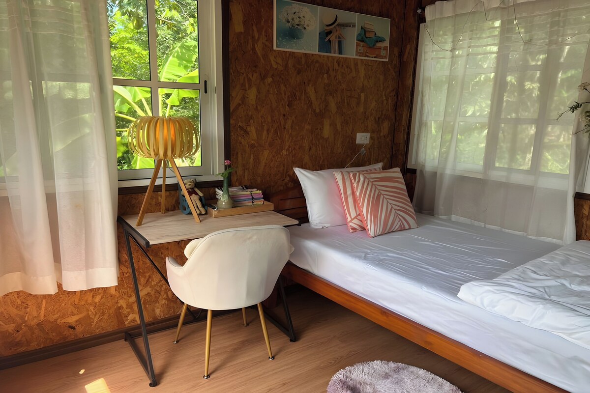 A cozy room with a wooden bed, a desk with a chair, and a window with sheer curtains.
