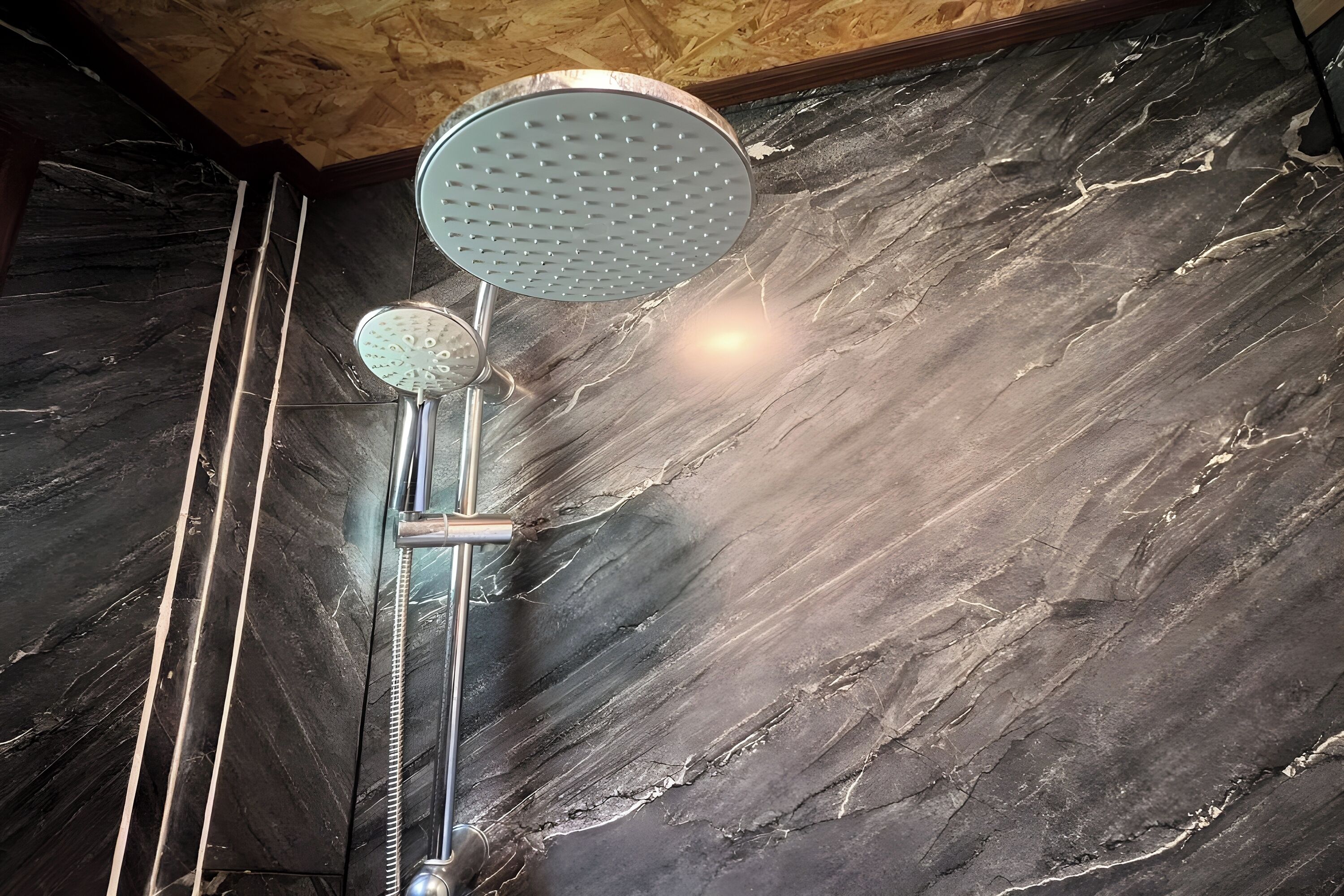 A shower with a rain showerhead and a handheld showerhead against a marble wall.