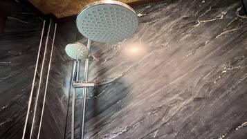 A shower with a rain showerhead and a handheld showerhead against a marble wall.