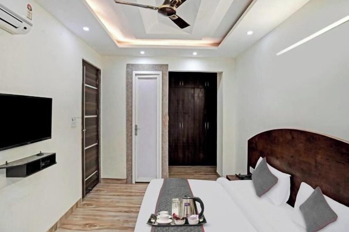 A modern hotel room with a flat-screen TV, a bed with a headboard, a tray with a coffee pot, and a wardrobe.