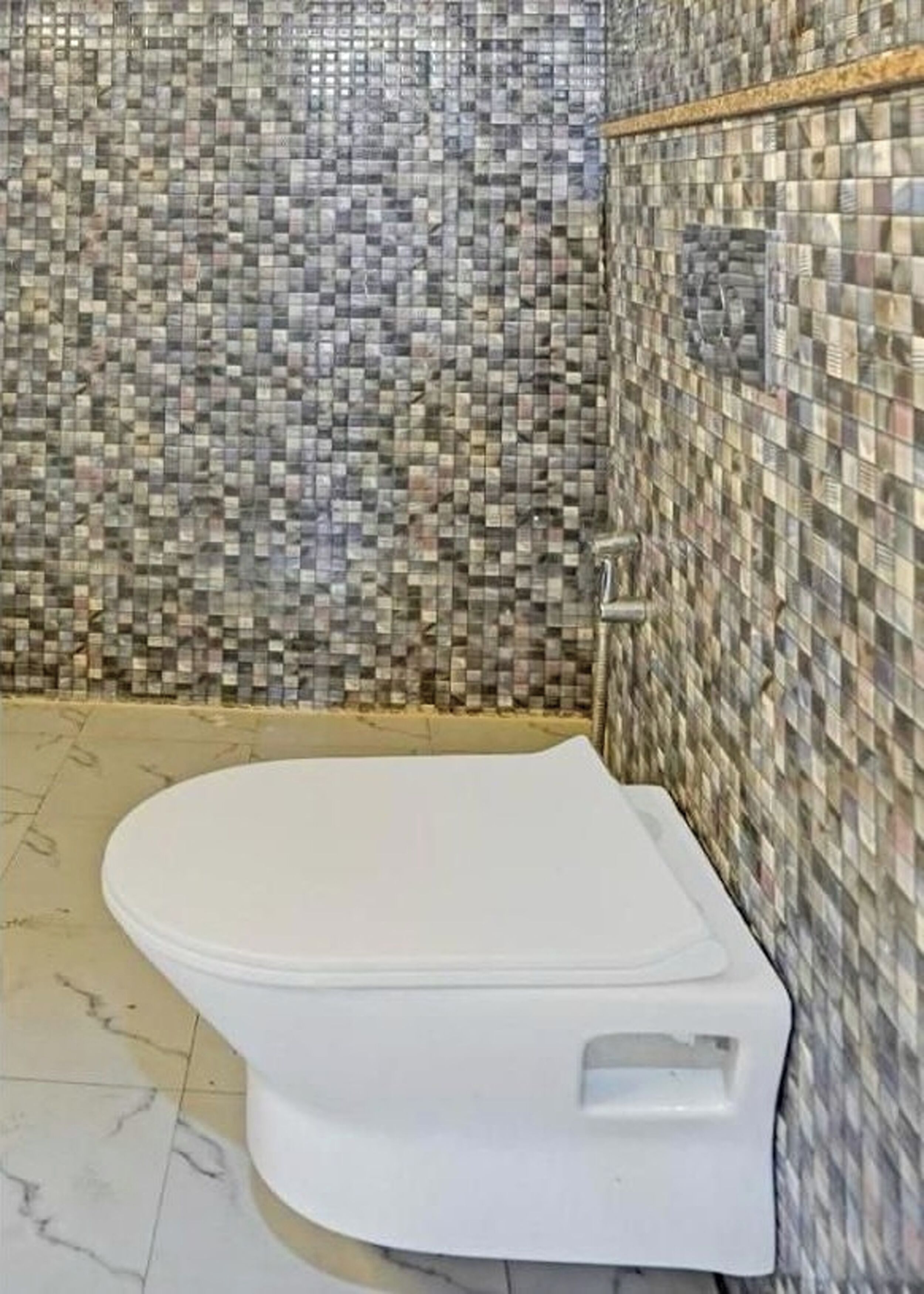 A bathroom with a toilet, tiled walls, and a marble floor.