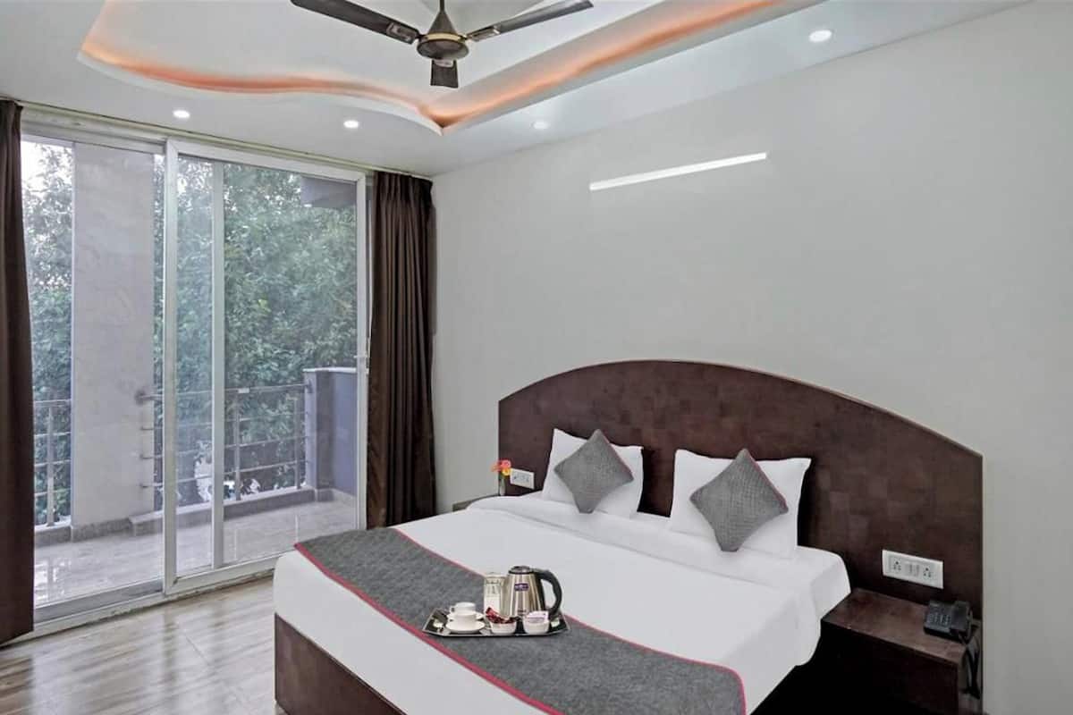 A hotel room with a large bed, a nightstand, a ceiling fan, and a view of greenery through the window.