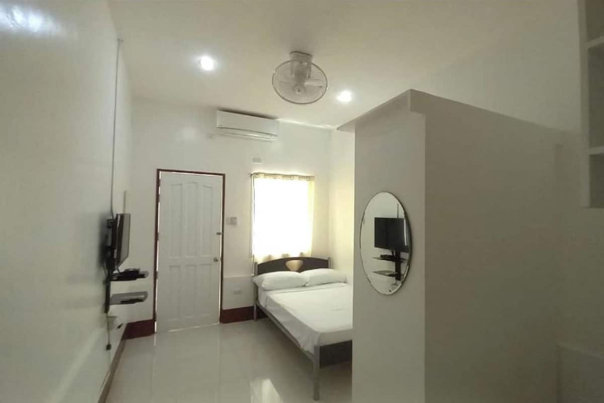A bedroom with a bed, a television, a mirror, and a door.
