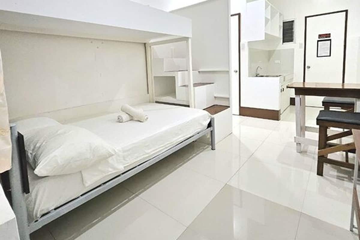 A compact hotel room with a single bed, a small desk, and a kitchenette.