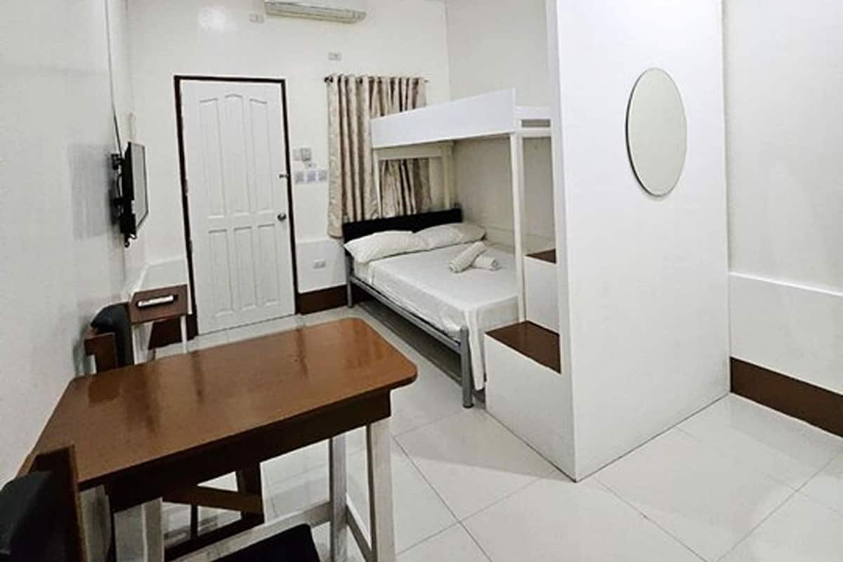 A compact room with a bunk bed, a small desk, a chair, and a bedside table.