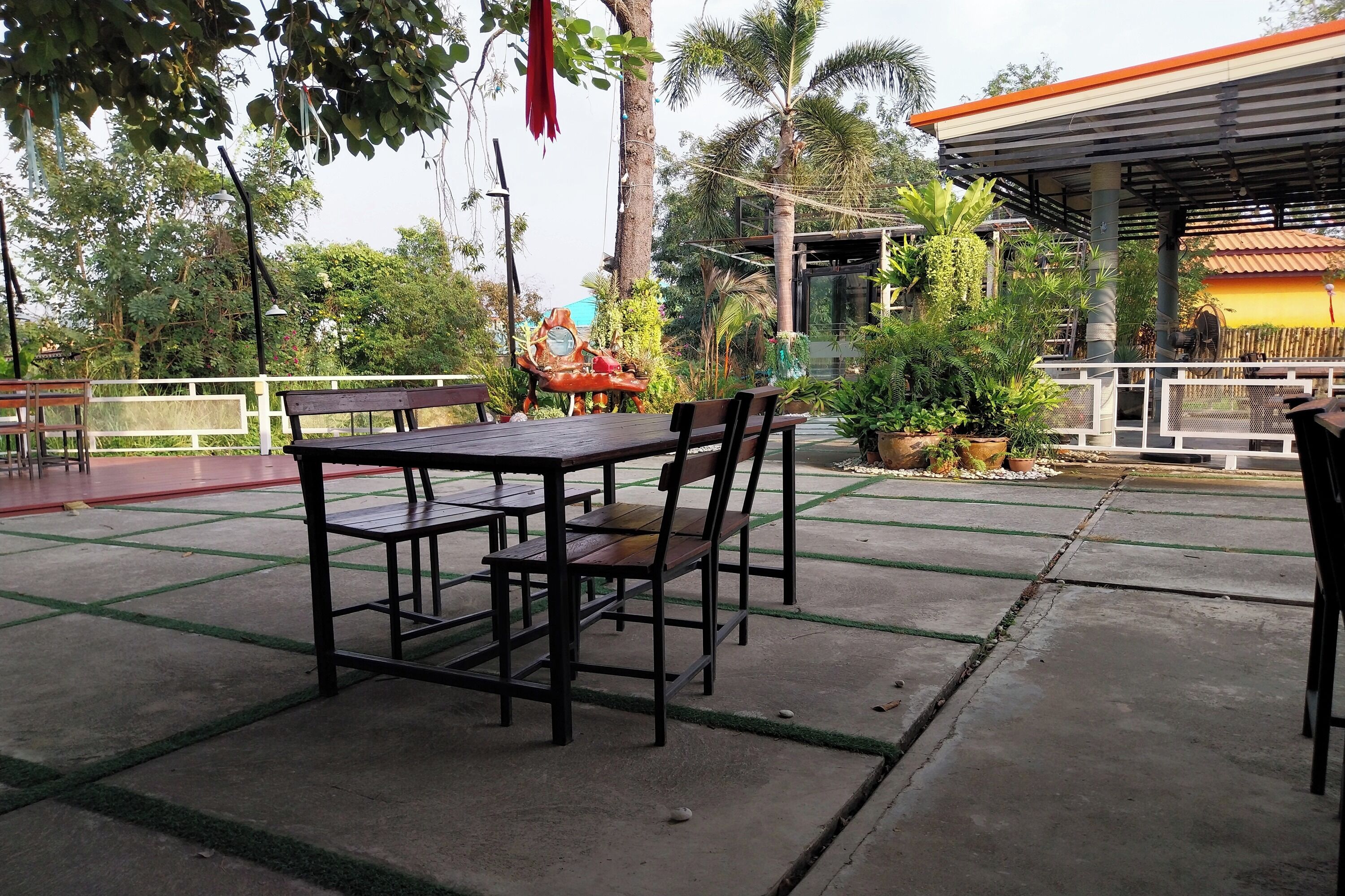 Zona de estar al aire libre con mesa y sillas, rodeada de follaje y una estructura cubierta.