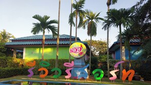 A colorful sign with Thai script and a welcome message, surrounded by palm trees and a building with a green roof. - Review Resort (Sattahip)