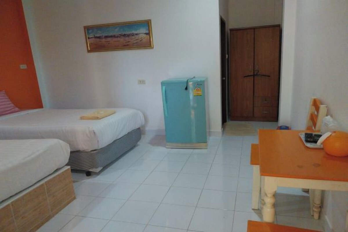 A bedroom with a bed, a small table, a refrigerator, and a door leading to another room.