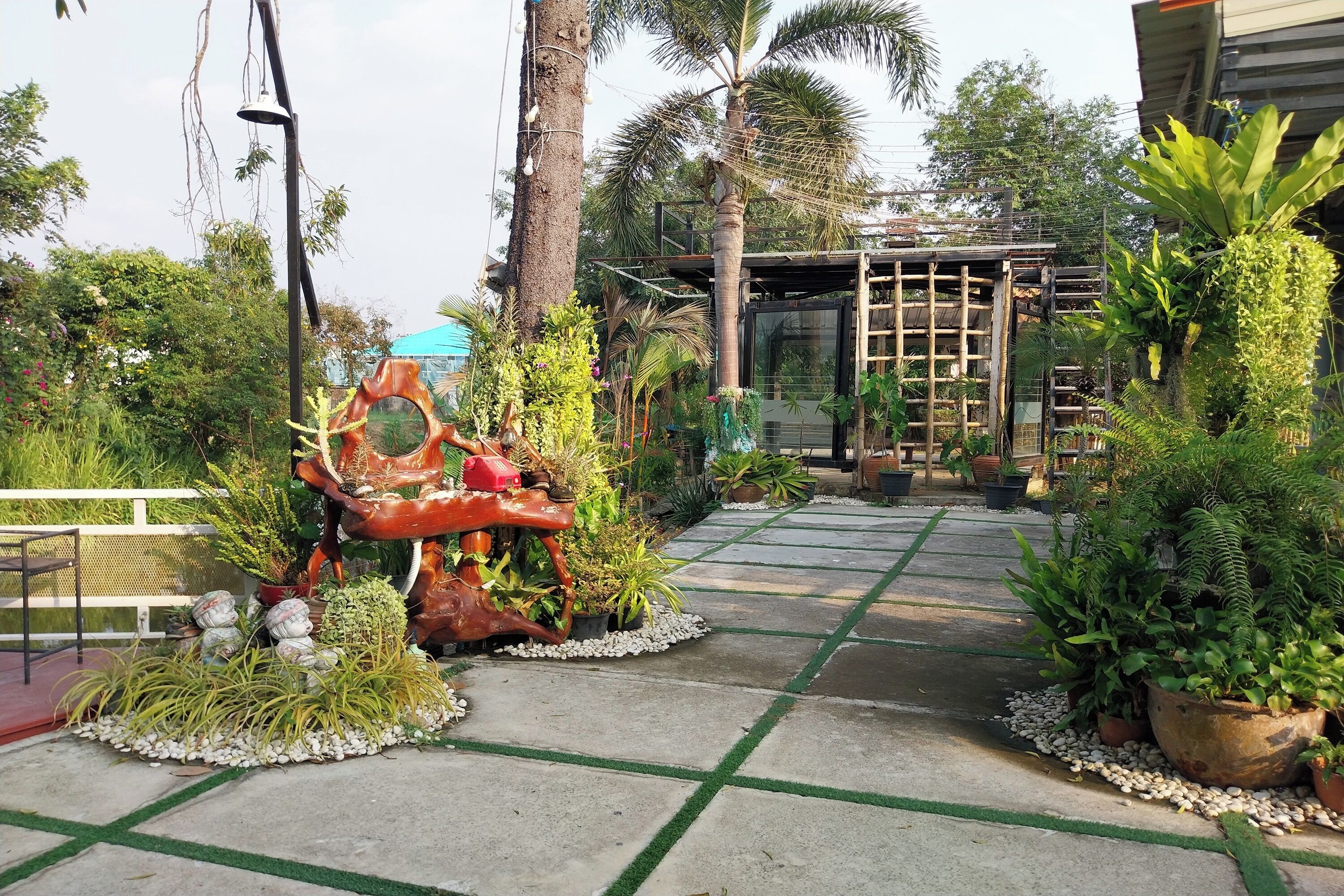 Un chemin de jardin bordé de plantes en pot et agrémenté d’une sculpture décorative.